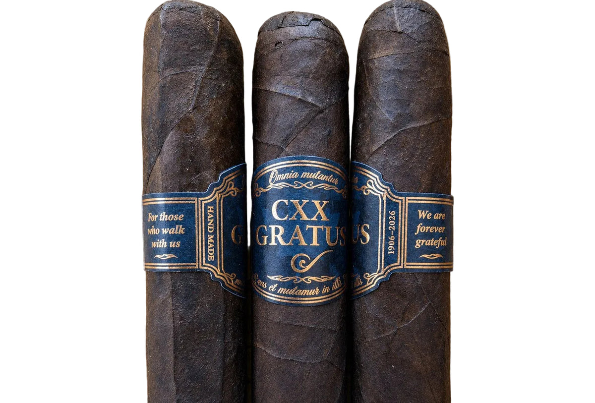 Three dark brown CXX Cigarrus cigars with blue and gold bands, arranged vertically on a light wood background.