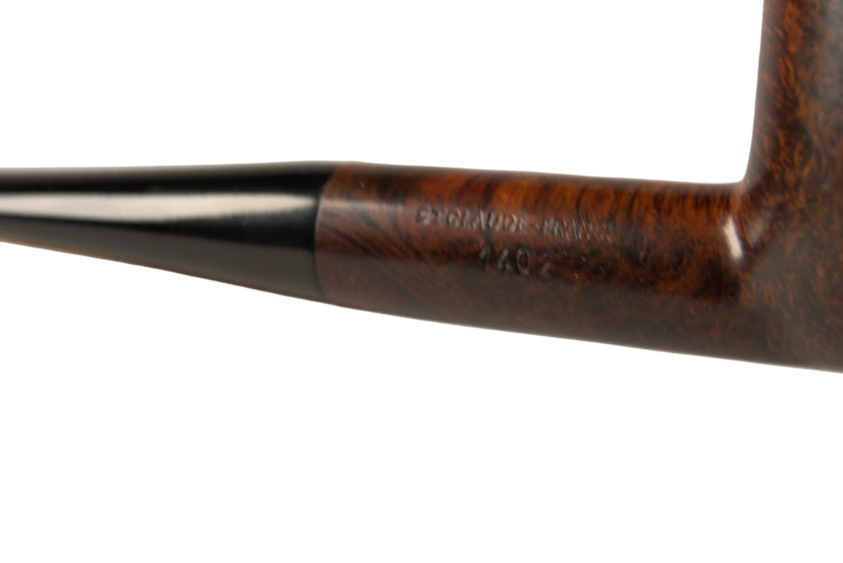 A close-up of a hand holding a dark brown wooden smoking pipe with a black stem, with a small wooden stand blurred in the background against a neutral light gray studio backdrop.