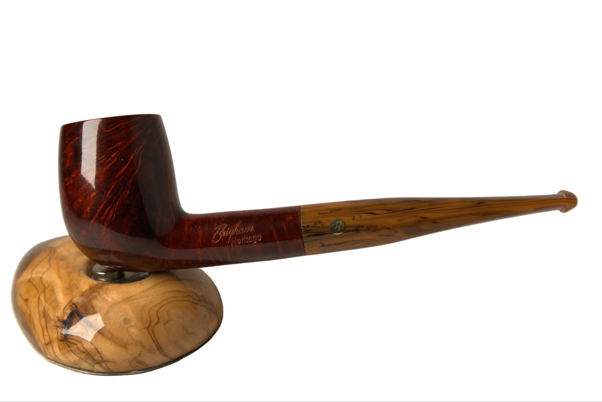A high-end smoking pipe with a dark reddish-brown wood bowl and a long, slender light brown wood stem, resting on a matching polished wood display stand against a neutral gray background.