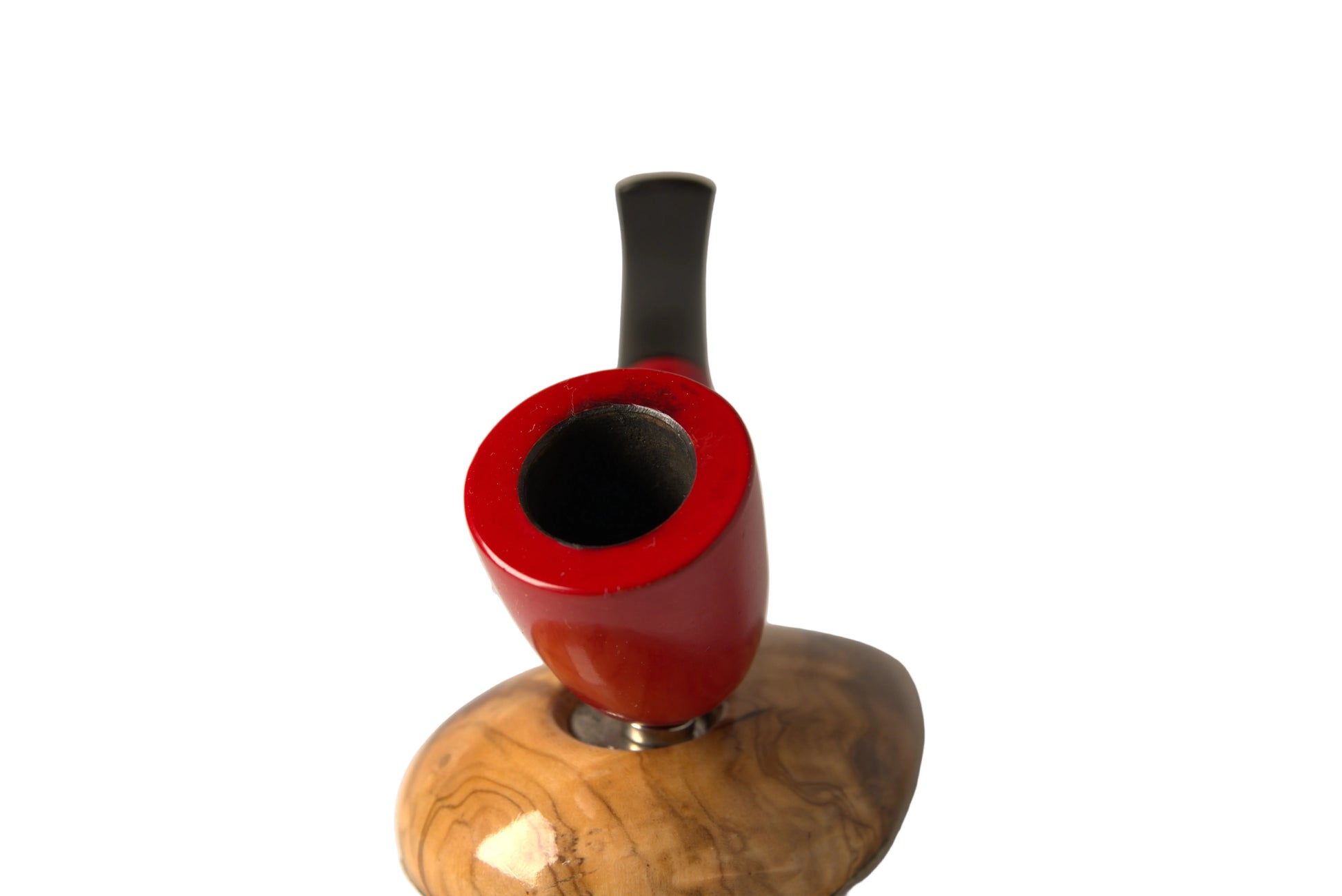 A close-up of a smoking pipe with a glossy red bowl and a curved black stem, resting on a polished wooden stand with a natural wood grain pattern, set against a neutral light gray background.
