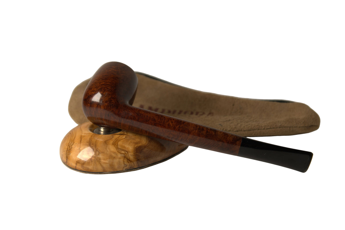 A smoking pipe with a dark brown burl wood bowl and a black stem, resting on a carved wooden stand with a tan suede pouch behind it, photographed on a neutral light gray background.