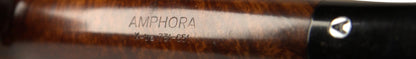 A close-up of a dark brown wooden smoking pipe with 'AMPHORA' engraved on the shank, resting on a tan leather stand against a neutral gray background.