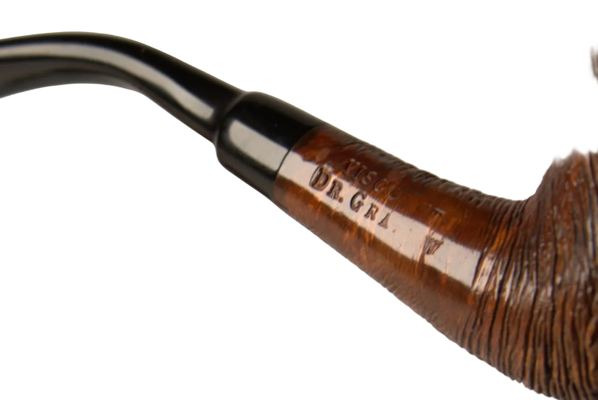 A close-up of a hand holding a carved brown smoking pipe with a black bowl, next to a small wooden stand on a neutral gray background.