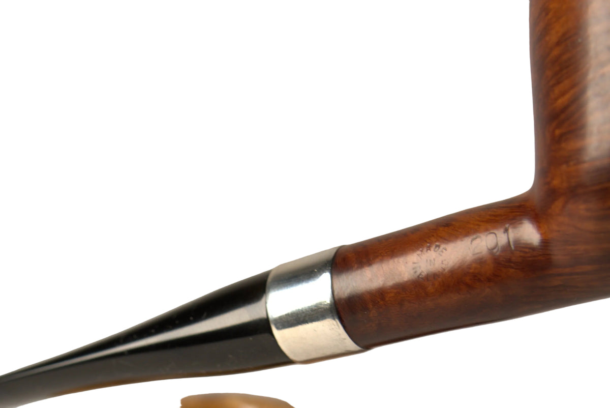 A close-up of a smoking pipe with a polished dark brown wooden bowl and a black bowl stem with a silver band, resting above a matching wooden display stand. A hand is holding the pipe, and the background is a clean, neutral studio gray.