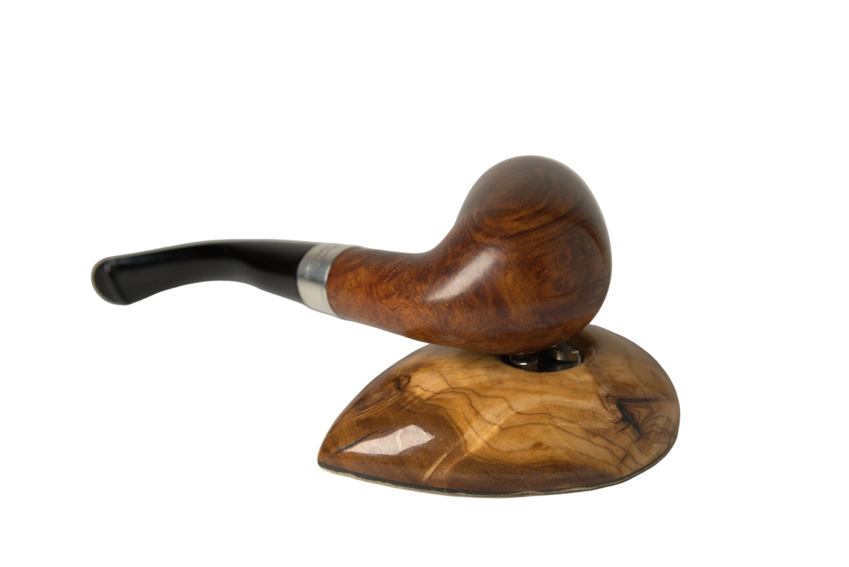 A smoking pipe with a polished brown wooden bowl, a silver ferrule, and a black stem, displayed on a matching carved wooden stand against a neutral light gray background.