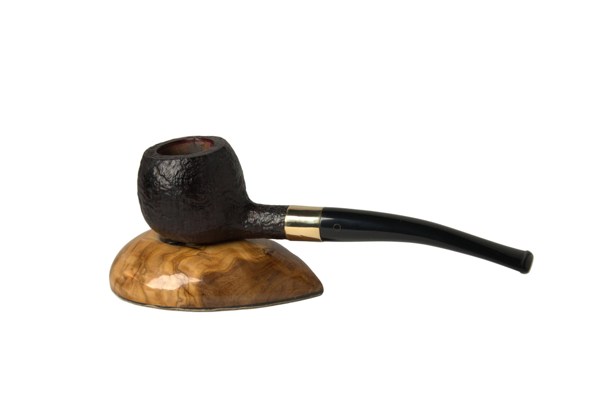 A dark brown textured smoking pipe with a long black stem and a gold band, resting on a polished wooden stand against a neutral gray background.