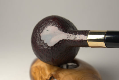 A close-up studio shot of a smoking pipe resting on a carved wooden stand against a neutral light gray background.