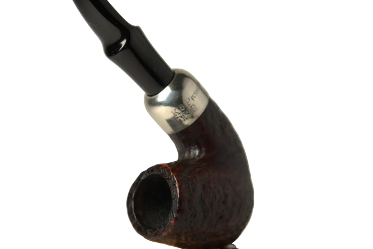 A smoking pipe with a dark brown carved wooden bowl, a silver metal band, and a black curved stem, displayed on a polished light wood stand against a neutral gray background.