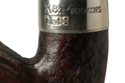 A close-up of a smoking pipe with a dark brown carved wood bowl and a black stem, featuring a polished silver band engraved with 'M. H.