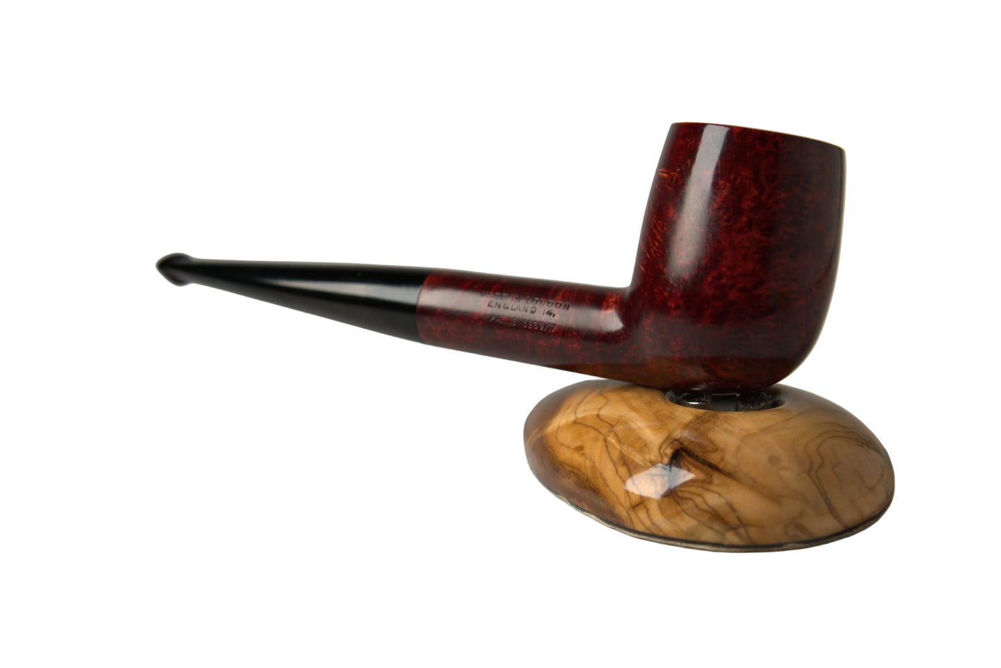 A smoking pipe with a dark reddish-brown carved wood bowl and stem, resting on a polished natural wood stand against a neutral gray background.