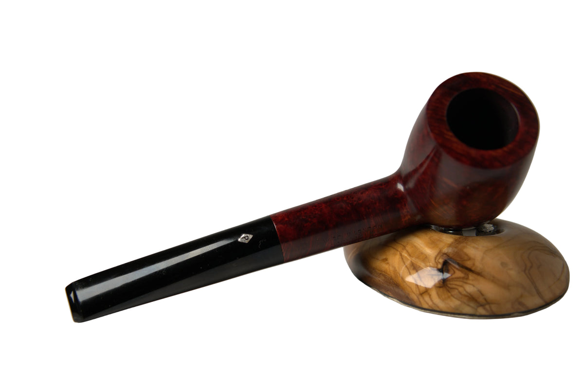 A premium smoking pipe with a glossy dark reddish-brown wood bowl and a black stem, resting on a matching carved wooden stand against a neutral gray background.