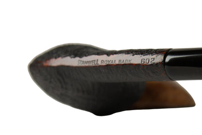 A close-up of a smoking pipe with a black handle and a dark brown textured bowl, resting on a white surface with a soft gray background.