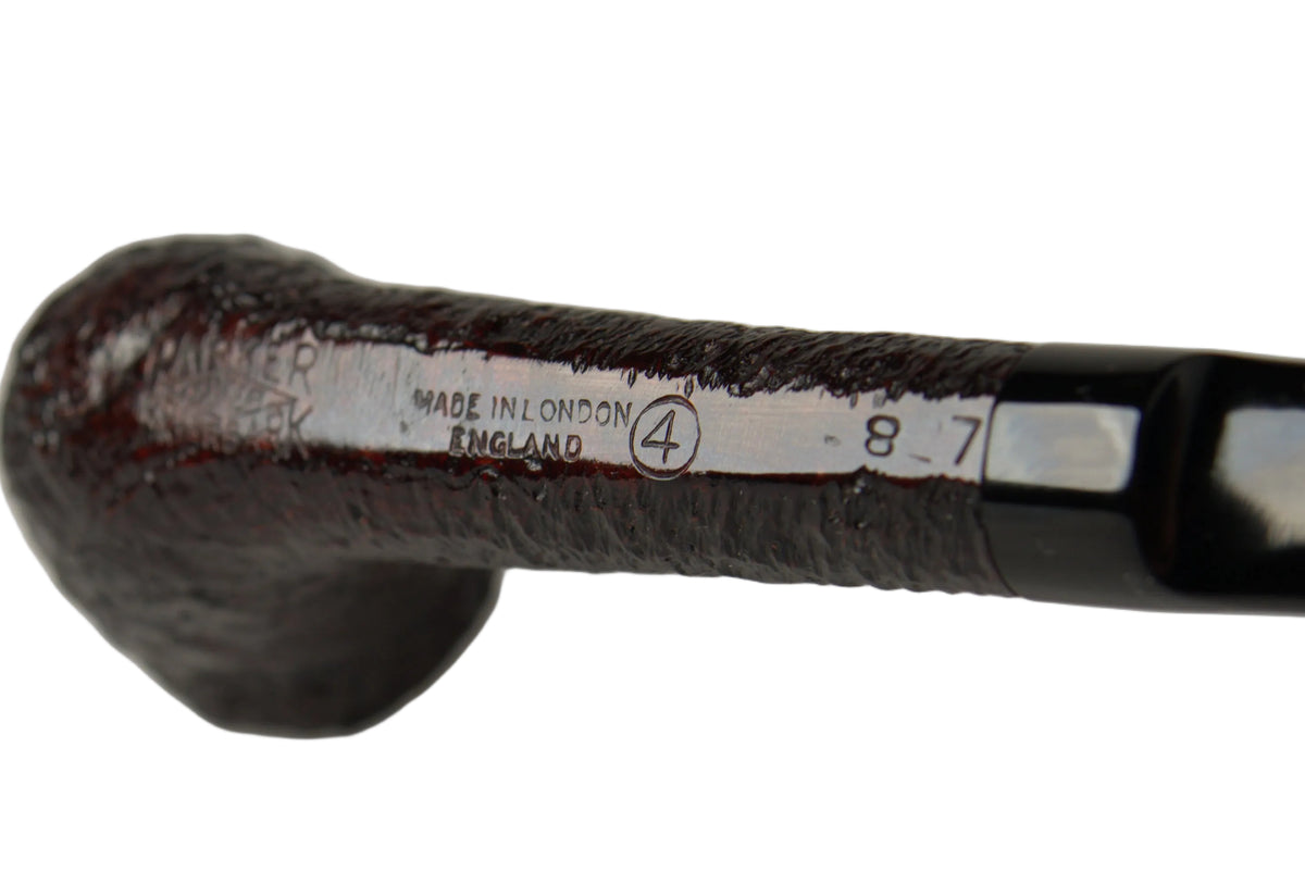 A close-up of a dark brown wooden smoking pipe with a black handle, held by a hand. The pipe has a white paper band near the base with engraved text reading 'MADE IN LONDON ENGLAND' and a serial number '8 7'.