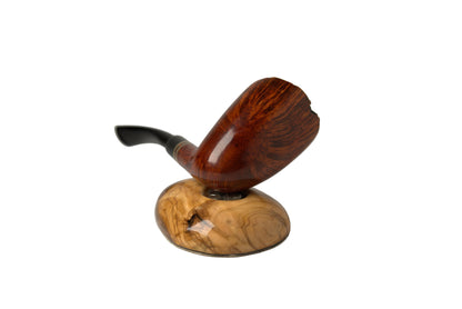 A polished wooden smoking pipe with a dark stem, resting on a carved wooden display stand against a neutral gray studio background.