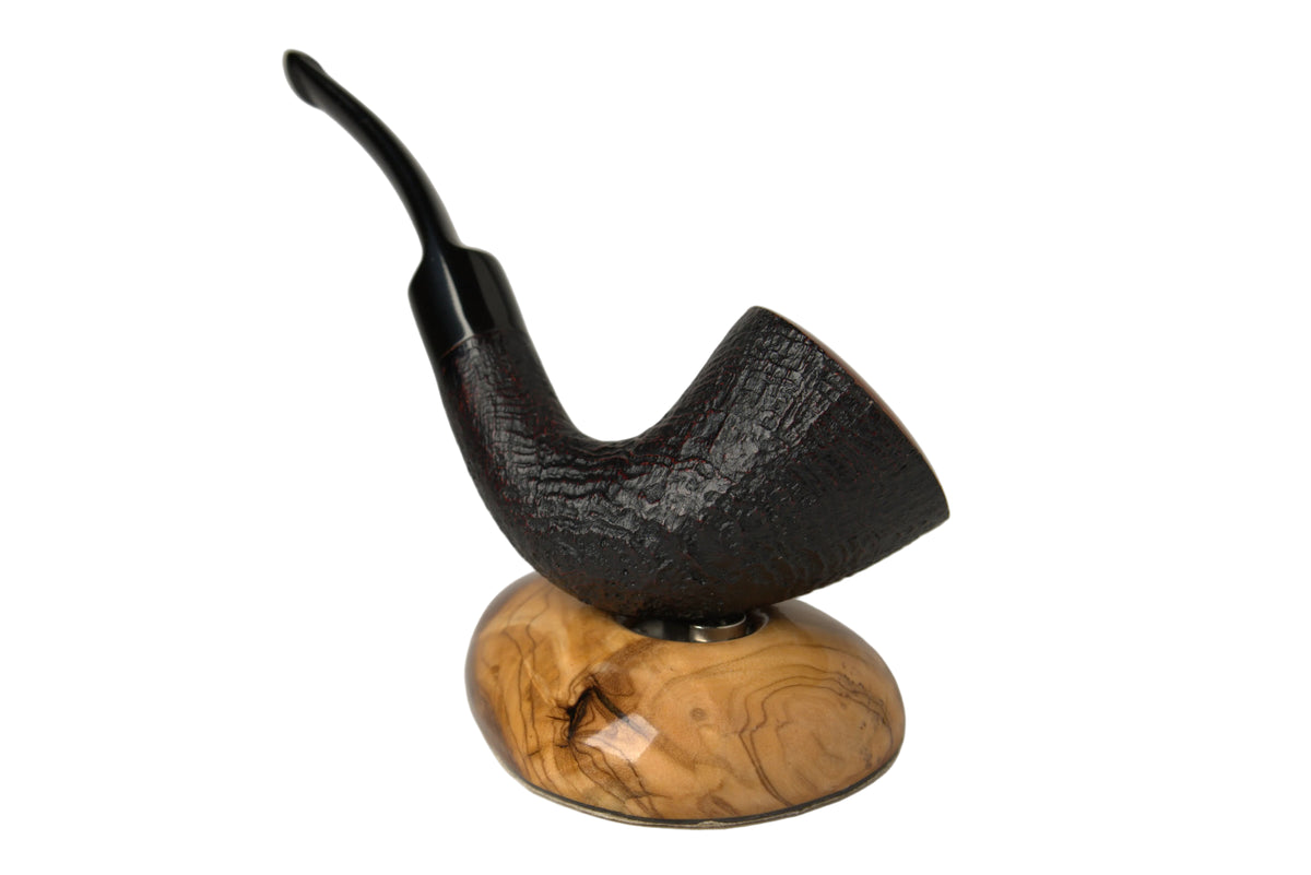 A dark brown smoking pipe with a textured finish, mounted on a polished oval wooden base with a swirling grain pattern, set against a neutral gray background.