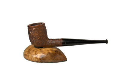 A carved brown smoking pipe with a long black stem, displayed on a polished burl wood stand against a neutral gray background.