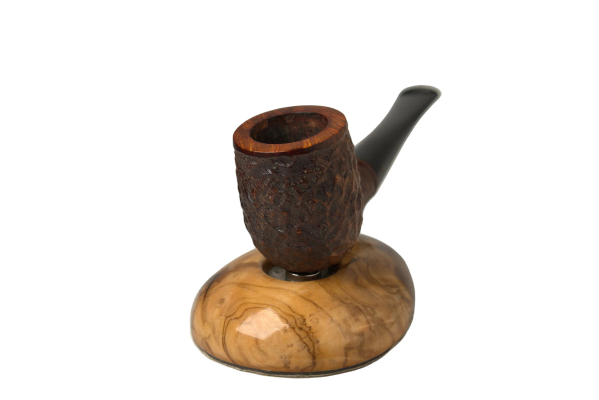A smoking pipe with a dark brown textured bowl and a curved dark stem, resting on a polished light brown wooden stand against a neutral gray studio background.