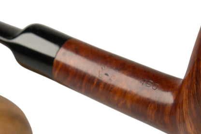 A hand holding a brown wooden smoking pipe with a black stem, with a matching wooden tobacco box blurred in the background on a light gray studio surface.