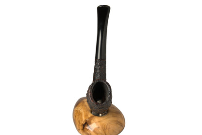 A smoking pipe with a dark, textured stem and bowl, mounted on a polished light brown wood base, photographed against a neutral gray background.