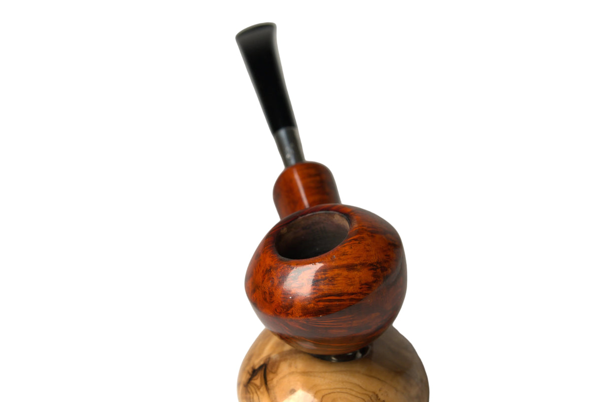 A handcrafted smoking pipe with a polished reddish-brown wooden bowl and stem, resting on a dual-tier wooden display stand against a neutral gray background.