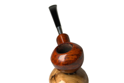 A handcrafted smoking pipe with a polished reddish-brown wooden bowl and stem, resting on a dual-tier wooden display stand against a neutral gray background.