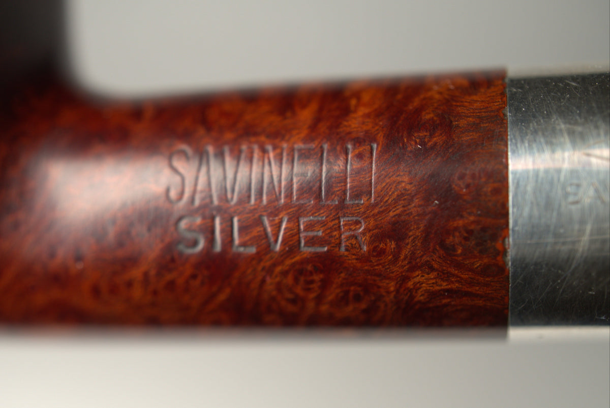 Close-up of a Savinele Silver smoking pipe showing the polished brown burl wood bowl and a silver metal stem against a light gray background.