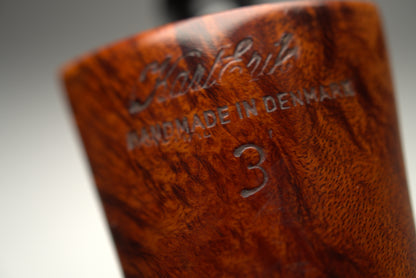 Close-up of a handcrafted wooden smoking pipe body with a richly figured brown wood grain, featuring engraved text that reads 'Kolding HANDMADE IN DENMARK' and a size '3'.