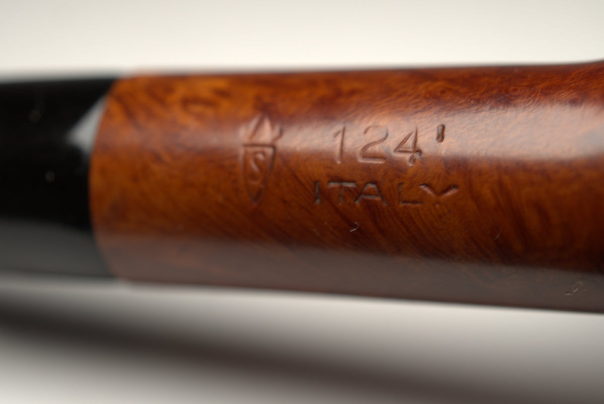 Close-up of a wooden smoking pipe showing a polished brown wood body with an engraved logo and '124 ITALY' text, connected to a black bowl, on a neutral gray background.