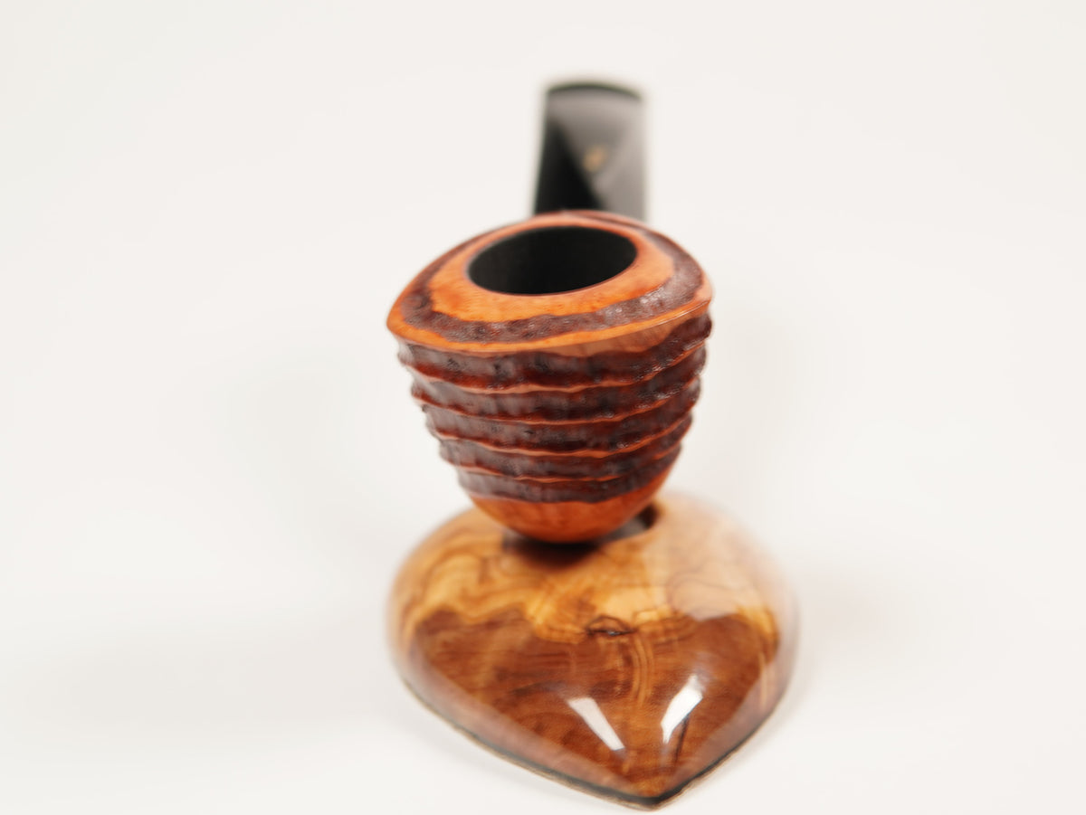 A close-up of a smoking pipe with a carved wooden bowl and a dark stem, set against a plain white background.