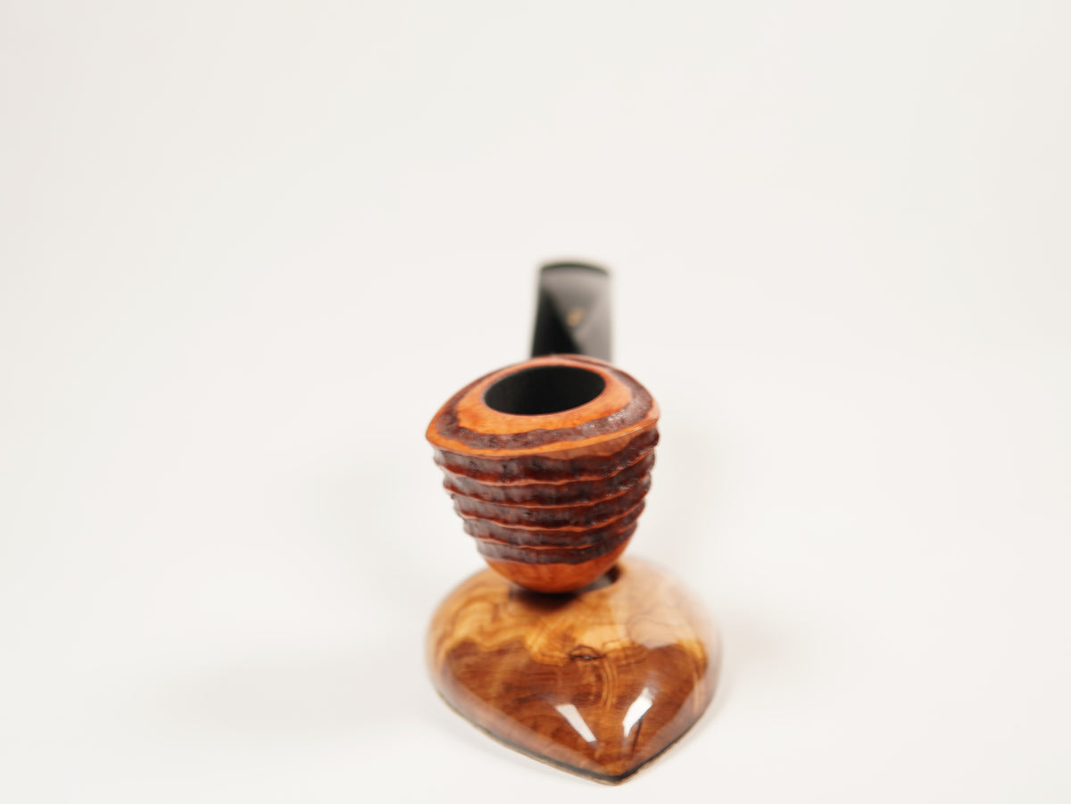 A close-up of a smoking pipe with a carved wooden bowl and a dark stem, set against a plain white background.