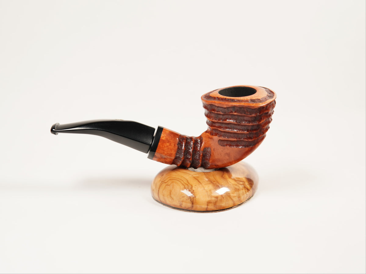 A carved smoking pipe with a curved black stem and a ribbed brown wooden bowl, displayed on a polished oval wooden stand against a clean white background.