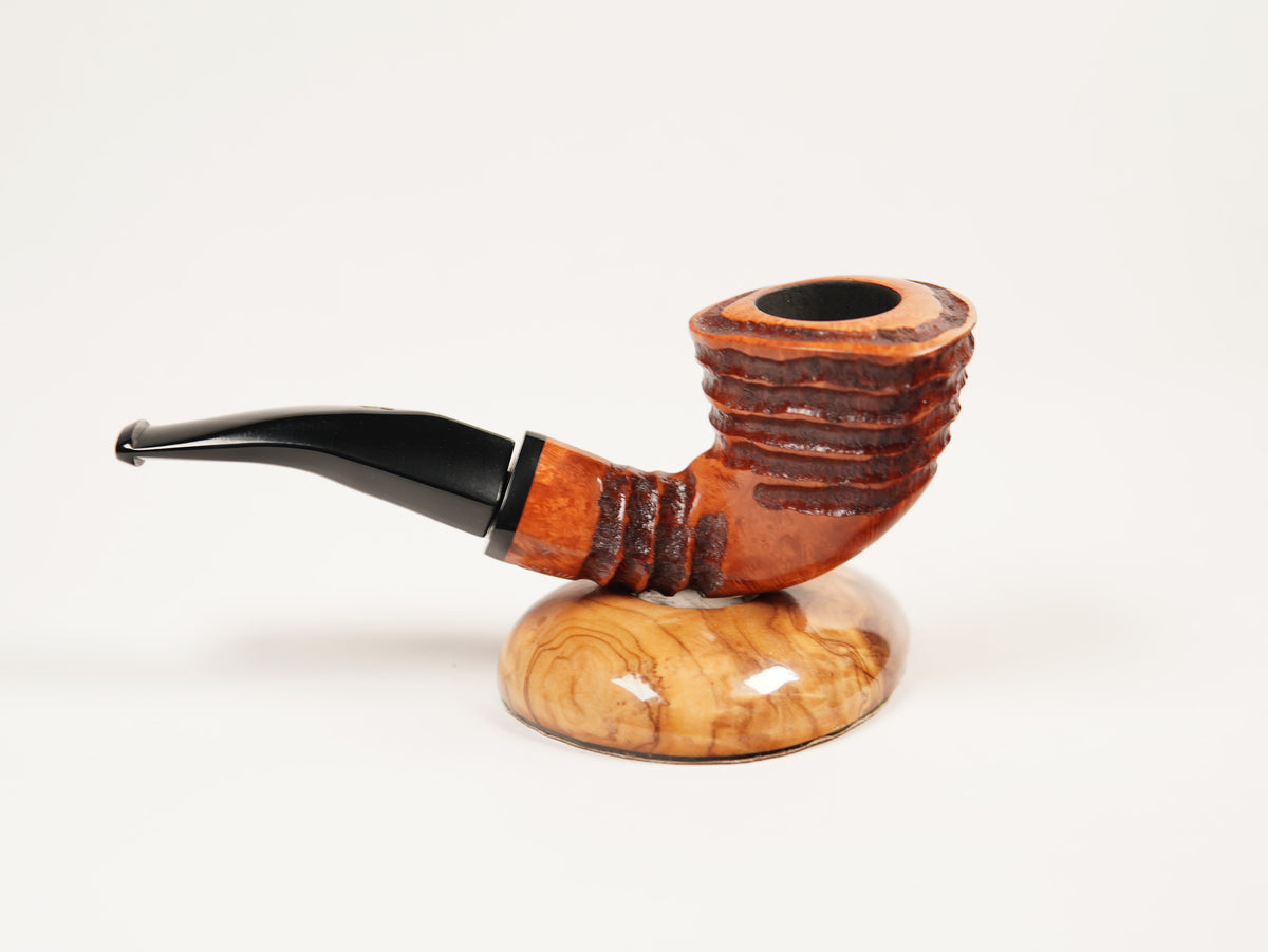 A carved smoking pipe with a curved black stem and a ribbed brown wooden bowl, displayed on a polished oval wooden stand against a clean white background.