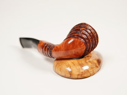 A polished wooden smoking pipe with a curved reddish-brown bowl and a black mouthpiece, resting on a matching carved wooden stand against a clean white background.
