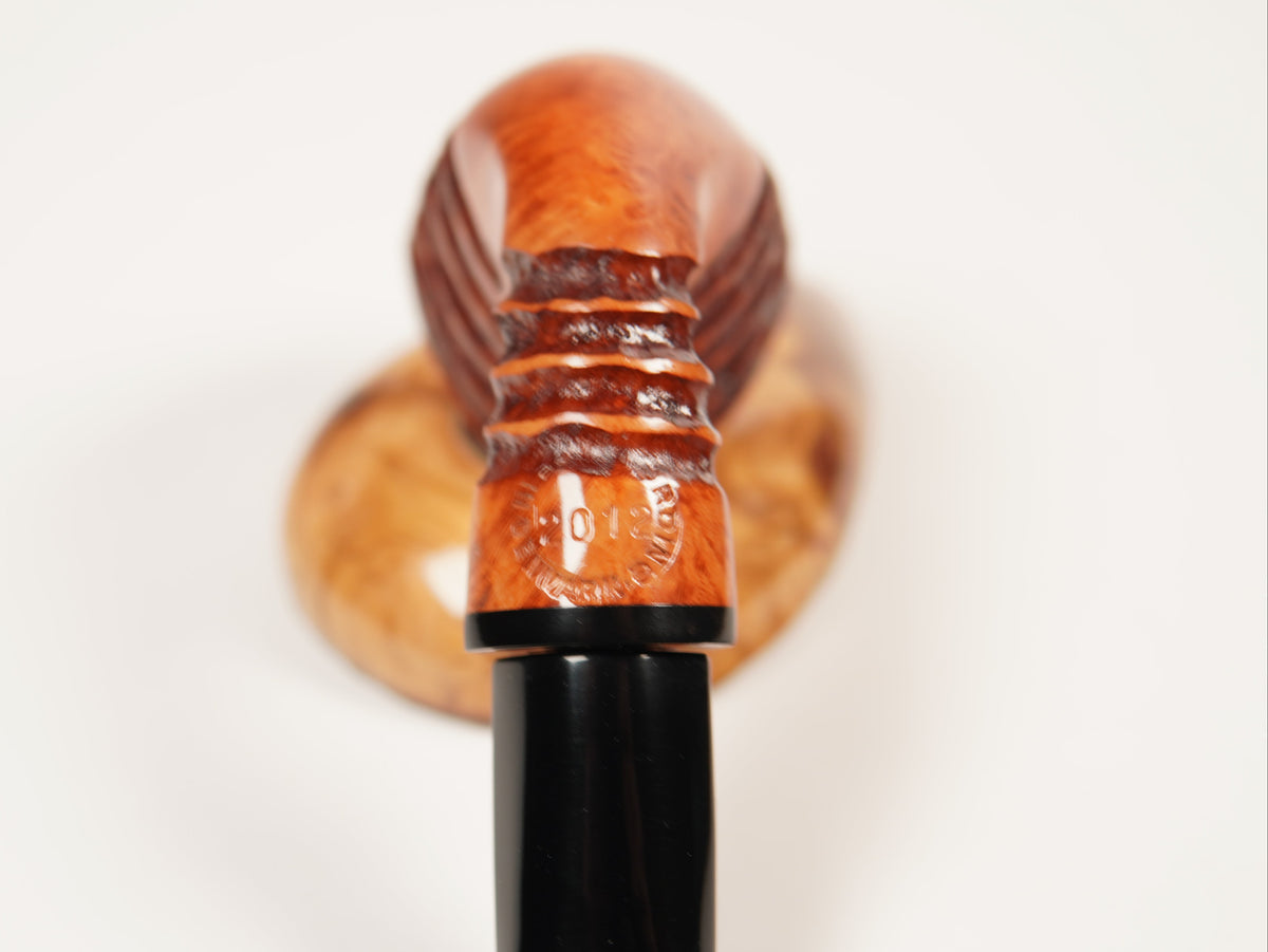 A close-up of a smoking pipe with a polished reddish-brown wooden bowl and a glossy black stem, set against a plain white background.
