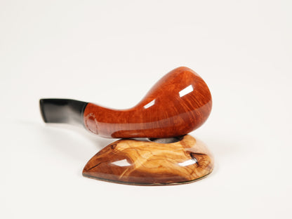A polished wooden smoking pipe with a glossy reddish-brown bowl and a black stem, resting on a matching carved wooden stand against a plain white background.