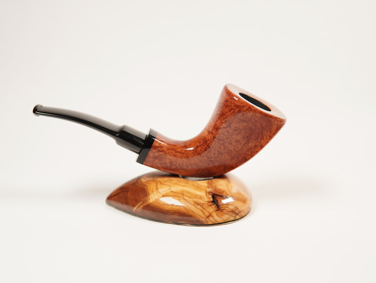 A polished smoking pipe with a curved reddish-brown wooden bowl and a dark stem, displayed on a matching carved wooden stand against a clean white background.