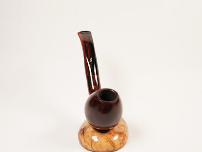A smoking pipe with a dark reddish-brown glossy stem and a round dark brown bowl, resting on a light tan wood base against a plain white background.