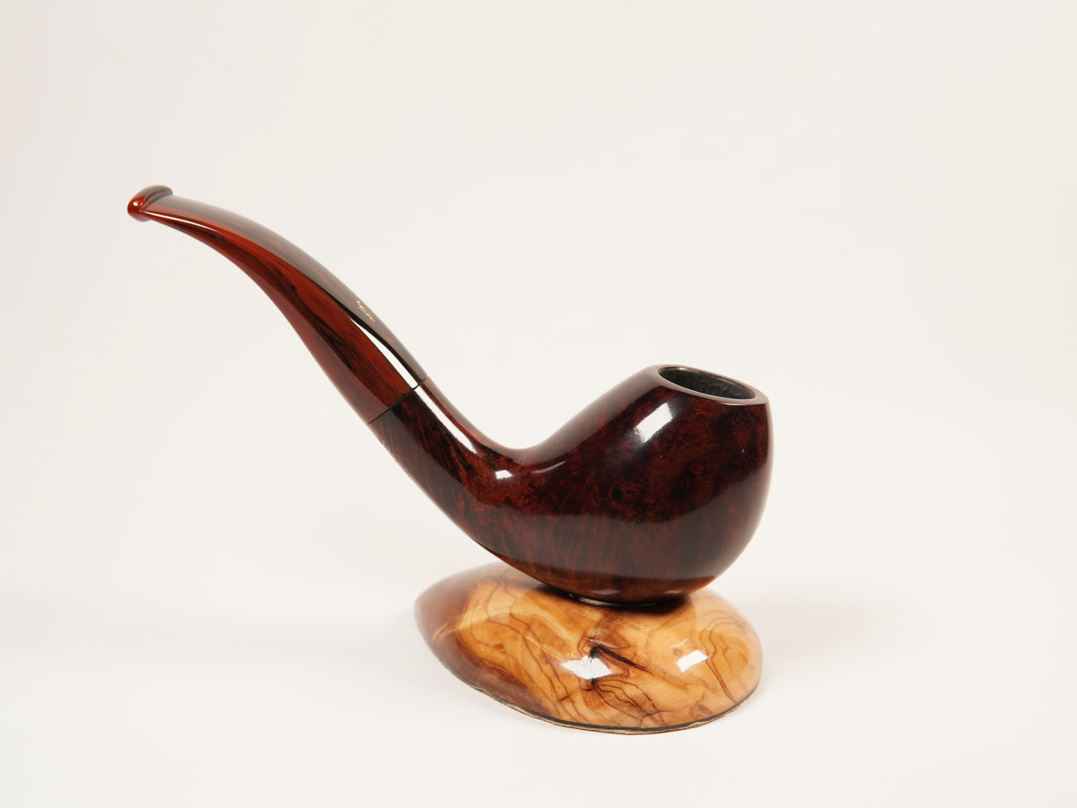 A polished dark brown wooden smoking pipe with a curved stem, displayed on a matching carved wooden base against a plain white background.