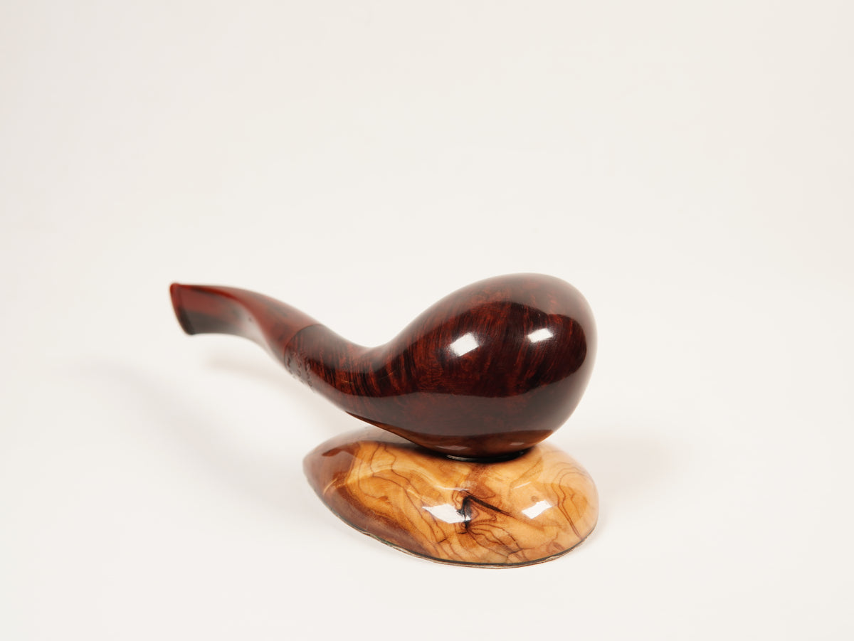 A polished wooden smoking pipe with a curved dark reddish-brown bowl and stem, resting on a matching carved wooden base against a plain white background.