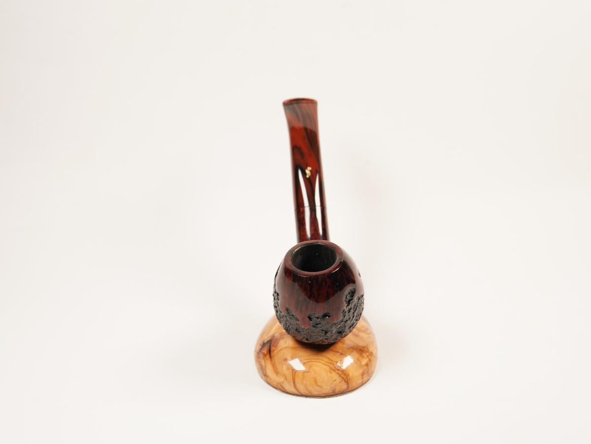 A smoking pipe with a dark reddish-brown carved bowl and a curved neck, resting on a polished light tan wood base against a plain white background.