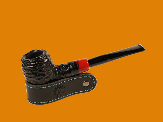 A black textured smoking pipe with a red band near the stem, resting on a black leather stand with blue stitching, photographed on a clean off-white background.