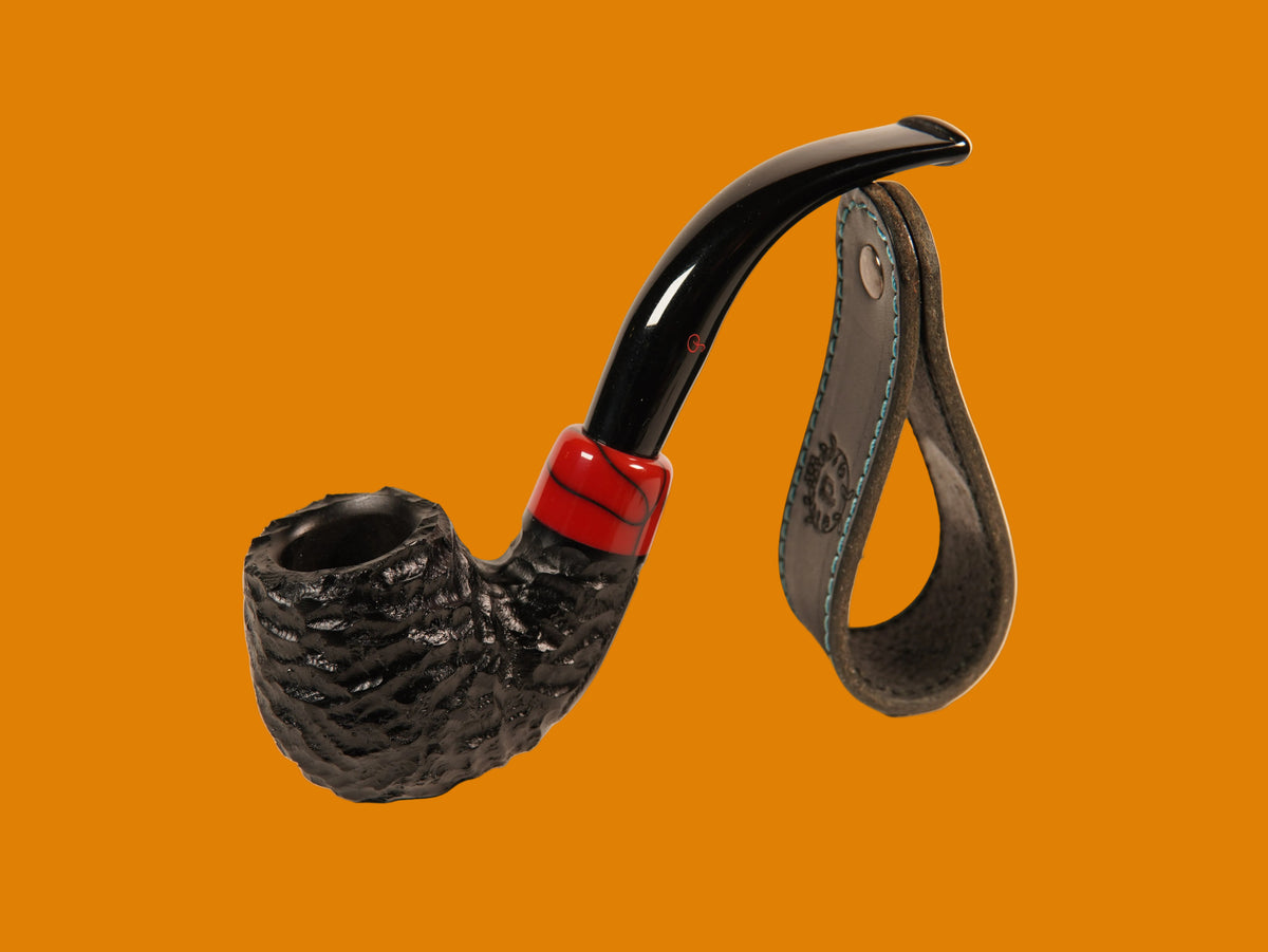 A smoking pipe with a dark textured bowl, glossy black curved stem, and a red band near the base, shown with a dark leather carrying strap on a plain light background.