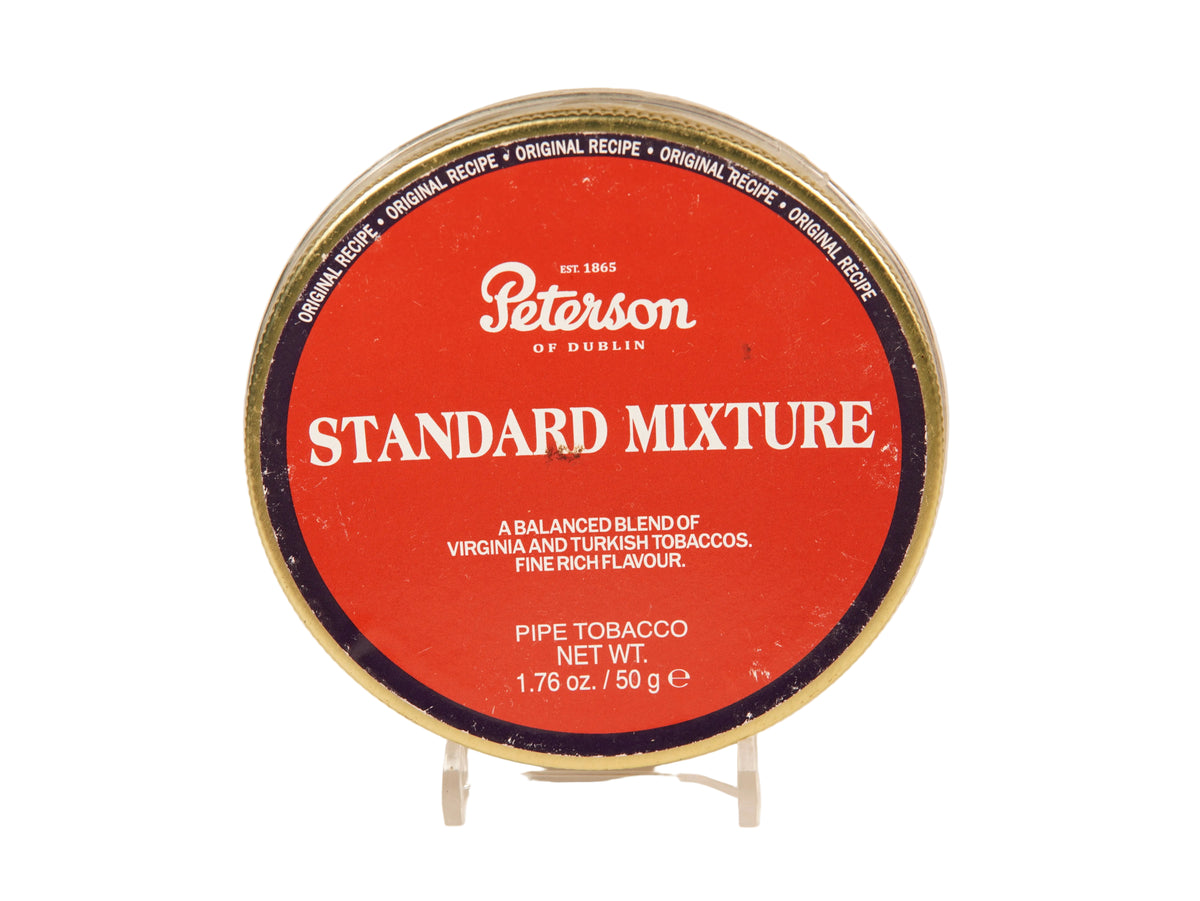 A round tin of Peterson of Dublin Standard Mixture pipe tobacco on a small clear display stand against a plain light background.