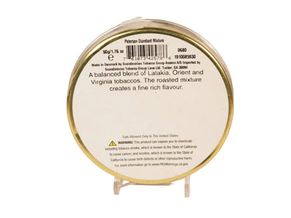 A round white paper label with black text and a barcode, mounted on a thin gold-colored metal rim, displayed on a small clear stand against a plain light background. The label reads 'Peterson Standard Mixture' and includes product details and warning information.