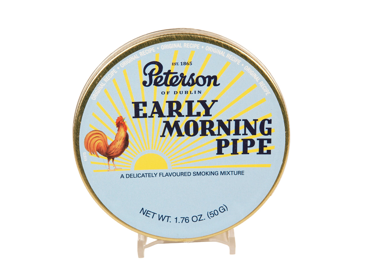 A round tin of Peterson of Dublin Early Morning Pipe smoking mixture, displayed on a small clear stand against a plain light background. The label features a light blue background with yellow sun rays, a rooster illustration, and dark blue text.