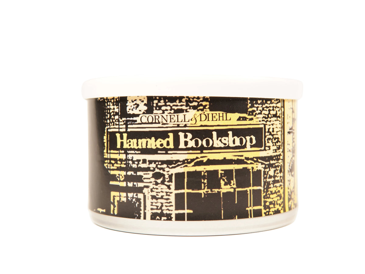 A white plastic jar candle with a black and gold label depicting a haunted bookshop storefront, labeled 'Cornell & Diehl Haunted Bookshop'.