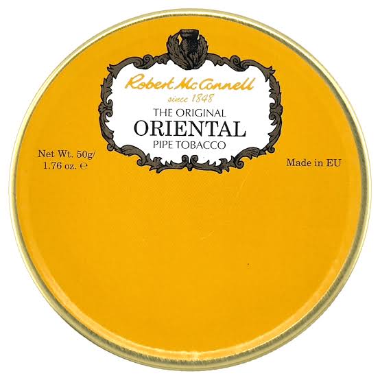 A round tin of Robert McCannell The Original Oriental Pipe Tobacco, showing a bright yellow-orange lid with a white and black central label and gold-toned rim on a white background.